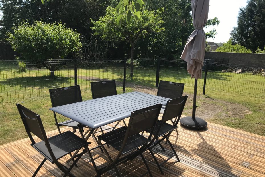 Un coin jardin avec 6 chaises et un parasol.